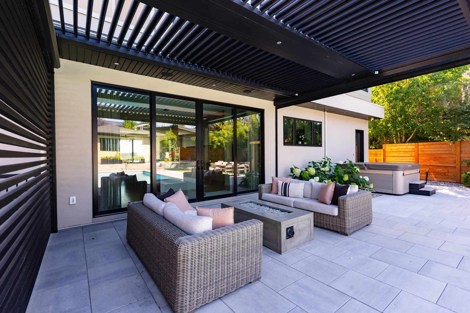 A covered patio under a louvred pergola, with an outdoor seating group and a fire table.