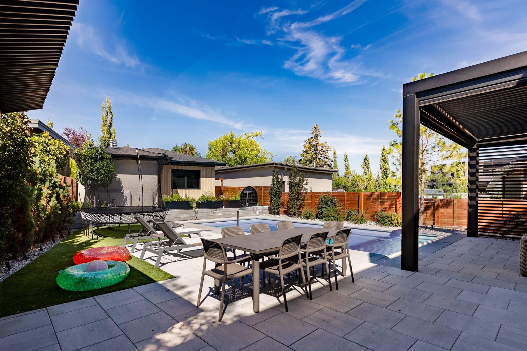 An outdoor dining table under a pergola beside the pool.