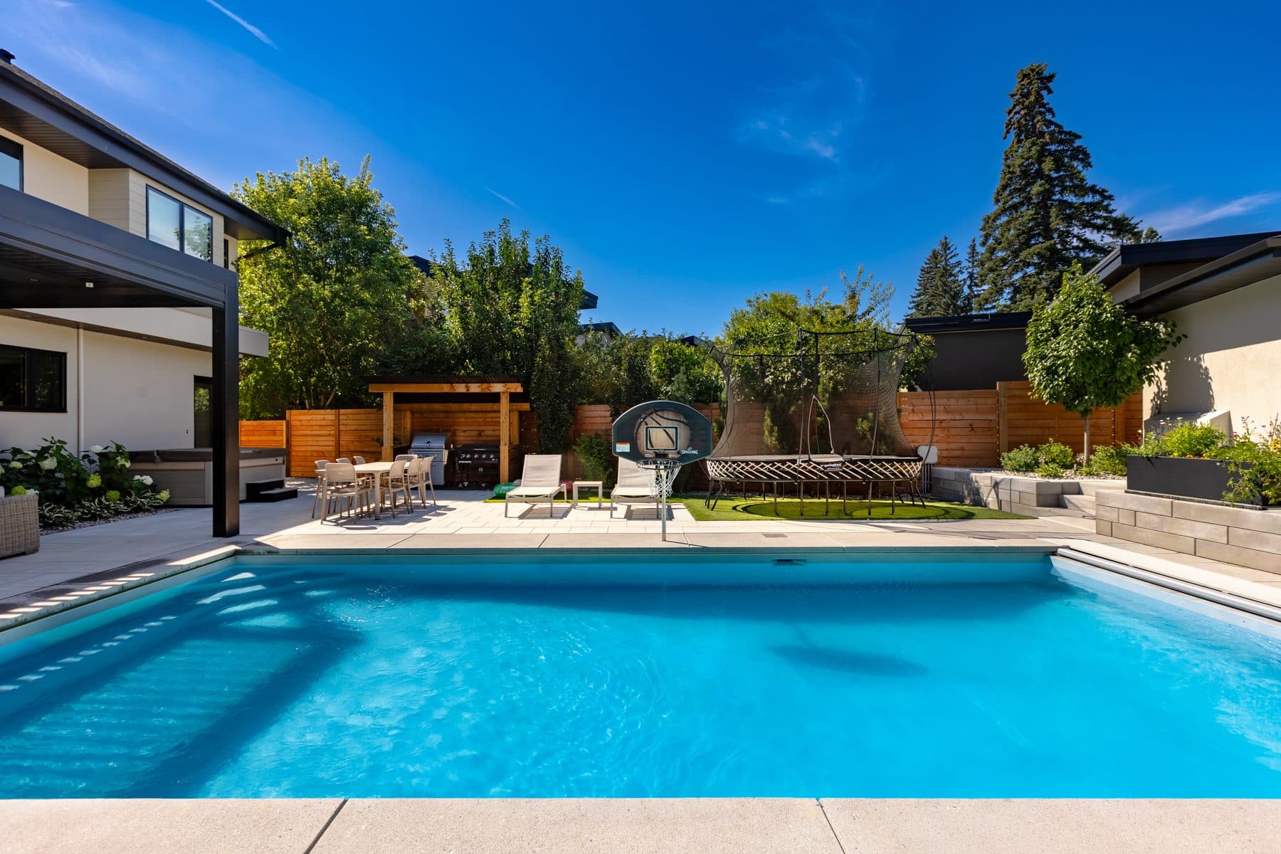 A rear yard seen wide — pool, stone terrace and the house behind it.