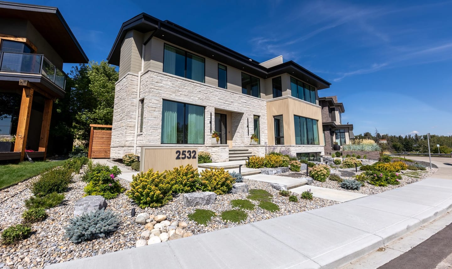 A contemporary Calgary house in pale stone and dark metal, seen at an angle from the street.