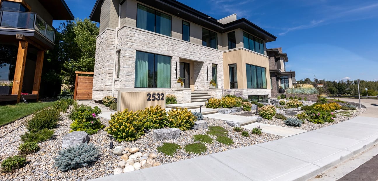 A contemporary Calgary house in pale stone and dark metal, seen at an angle from the street.